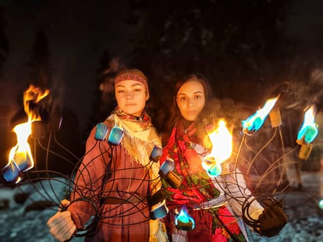 Vibrant actors perform an awe-inspiring fire show in ethnic costumes amidst a cold winter night, captivating the audience with their skill.