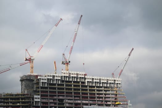Cranes operate at a construction site in Paris, where workers are actively involved in the development of a modern high-rise building under overcast weather.