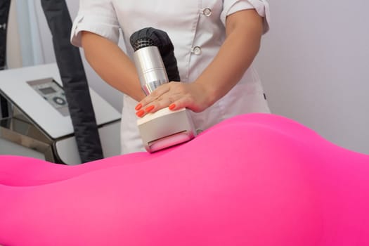Crop anonymous masseur massaging body of unrecognizable female client in anti cellulite suit with modern apparatus in clinic