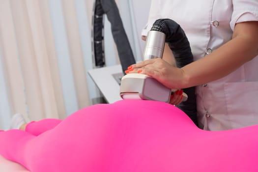 Crop anonymous masseur massaging body of unrecognizable female client in anti cellulite suit with modern apparatus in clinic