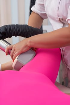 Crop anonymous masseur massaging leg of unrecognizable female client in anti cellulite suit with modern apparatus in clinic