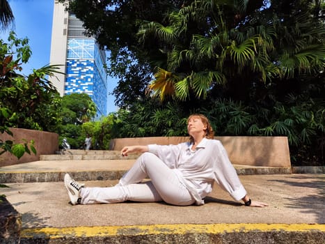 Blonde woman lies back on a stone path, surrounded by greenery, while savoring a peaceful moment during her travel adventure.