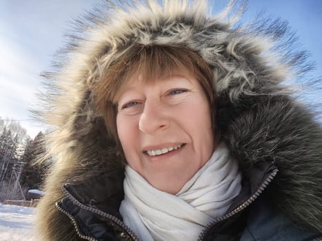 Middle aged woman in a cozy hooded jacket enjoys a sunny winter day while sharing her travel experiences.