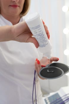 Crop unrecognizable masseuse in white medical robe electronic anti cellulite pads in modern clinic
