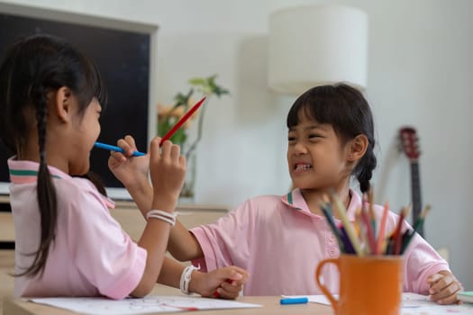 Two young friends share a playful interaction as they use colored pencils, highlighting the joy and spontaneity of childhood in a school setting.