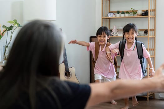 Two cheerful sisters, dressed in their school uniforms, rush into the living room to greet their grandmother, showcasing the joy of returning home after a day at school.
