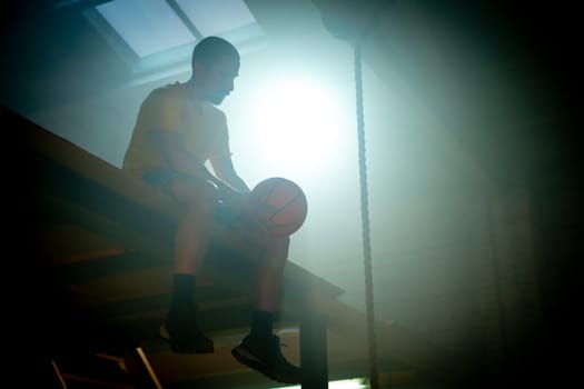A silhouette of a young basketball player sitting with a ball, surrounded by dramatic lighting effects.