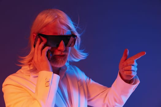 Confident businessman in sunglasses making a call and gesturing, set against a vibrant blue and purple background The image captures a sense of modernity and professionalism