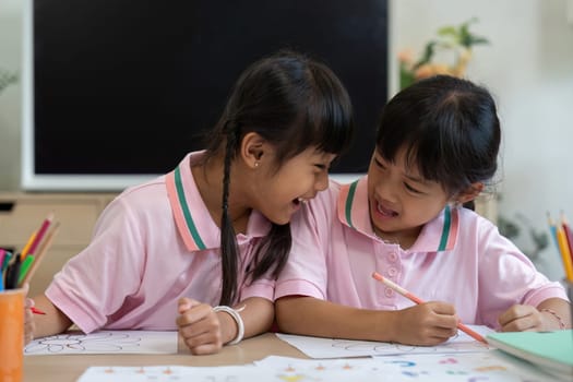 Two young friends share laughter and creativity as they color together, showcasing the joy of friendship and artistic expression in a classroom setting.
