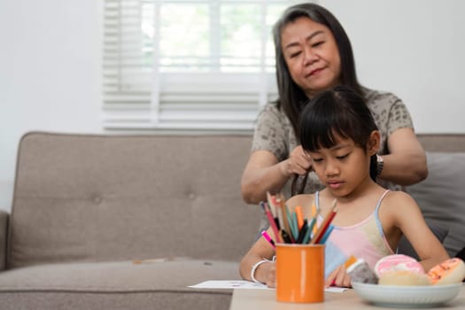 A tender moment as a grandmother styles her granddaughter's hair, reflecting love and care while the child engages in her creative drawing.