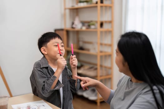 A young boy playfully holds colored markers while interacting with his mother, showcasing creativity and joy in their learning experience.