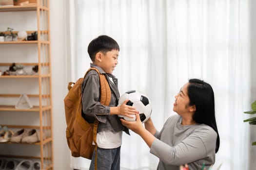 A mother joyfully hands a soccer ball to her son, who is ready for school. This moment reflects the balance of academics and sports in a child's life.