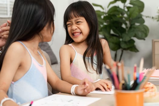 Two sisters enjoy a playful moment as they draw and share smiles, showcasing their bond and creativity in a cozy home environment.