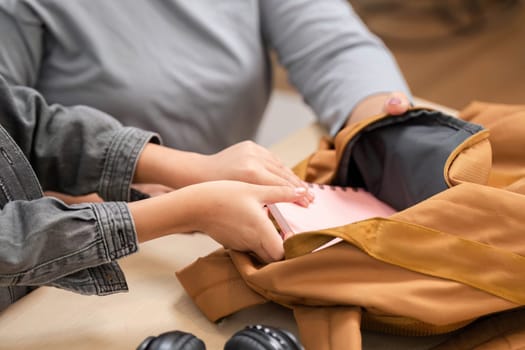 A young student enthusiastically places a notebook into their backpack, preparing for the upcoming school year. This image captures the excitement of back-to-school preparations.