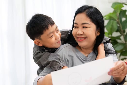 A mother and her son enjoy a creative moment together, with the boy showing off his drawing while sharing laughter and warmth in their cozy home.