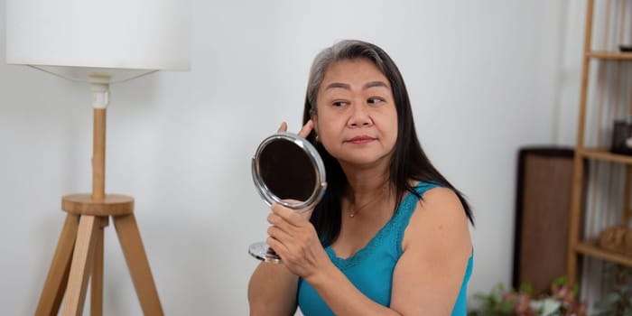 An elderly woman applies skincare while looking in the mirror, emphasizing the importance of beauty and self-care at any age. This image showcases a nurturing moment of personal care.