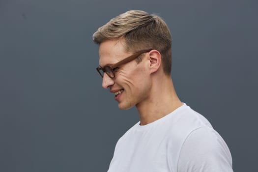 smiling man wearing glasses white t-shirt looking down in thoughtful mood isolated on plain gray background casual style mental health and gadgets concept representing digital detox and mindfulness