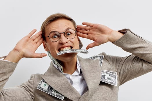 excited man with glasses in coat biting cash and holding hands near head isolated on white studio background showing success and enthusiasm related to digital nomad freelance lifestyle and remote work concept