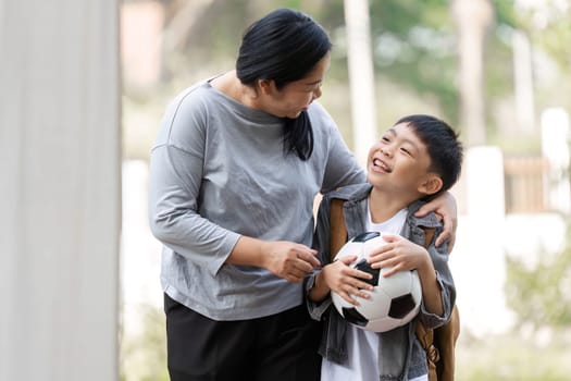 A mother smiles at her son as he holds a soccer ball, showcasing their bond and excitement for outdoor activities together.