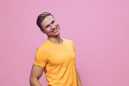 Smiling young man wearing bright orange t-shirt look camera with cheerful happy expression standing on pastel pink background. Casual fashion, positive emotion, relaxed pose digital nomad lifestyle concept.