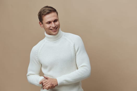 smiling caucasian man wearing white knitted turtleneck sweater looking to side with relaxed happy face against plain beige background. autumn cozy style and digital detox concept with casual warmth and comfort.