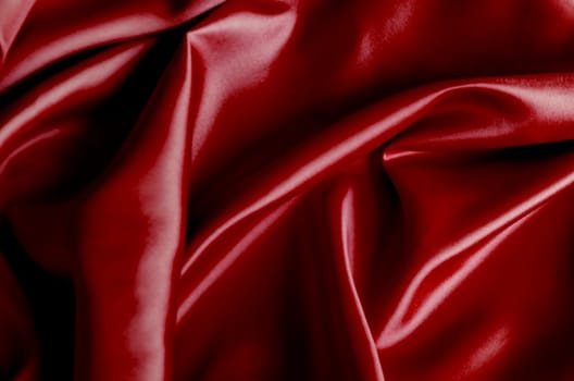 Top view of vibrant dark red fabric draped in soft, smooth waves with a glossy finish. Suitable for design and wallpaper background.