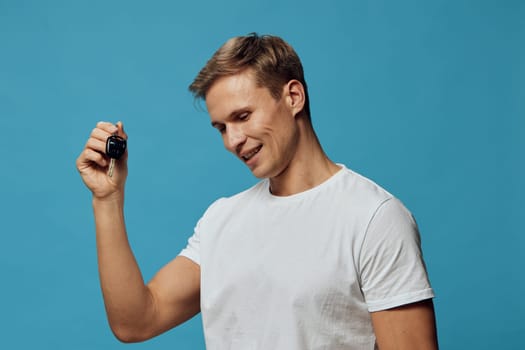 smiling man holding smart watch wearable fitness tracker in hand wearing white t-shirt looking down on blue background technology gadget digital device cyber security concept involving digital protection and innovation