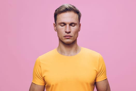 Calm man meditating with closed eyes wearing yellow t-shirt standing against pink background, focusing on mindfulness and mental health, promoting wellness and relaxation. Concept: mental health and mindfulness