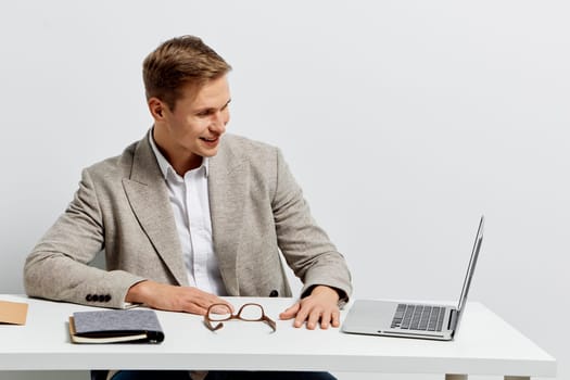 smiling man working with laptop in casual jacket sitting at desk with glasses and notebook, digital nomad lifestyle concept with technology and freedom ideas, isolated on white background