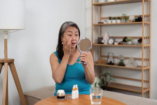 An elderly woman applies skincare while looking in the mirror, emphasizing the importance of beauty and self-care at any age. This image showcases a nurturing moment of personal care.
