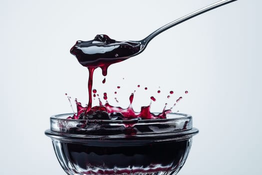 A glass jar filled with rich berry jam is depicted, with a spoon lifting out a scoop that causes droplets to splash. The scene captures the vibrant color and texture of the jam.