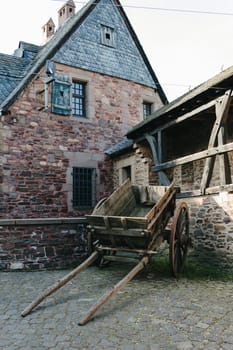 Beautiful view of old wooden medieval cart standing on stone square in old castle near stone building on spring day, side view close up. Concept of historical landmarks, time of travel and tourism.