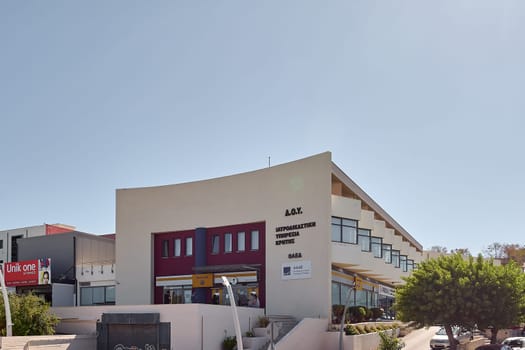 Crete.Greece - april 23, 2025: Contemporary forensic investigation facility with official signage on a sunny street, surrounded by trees and commercial establishments in an urban setting.