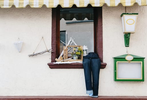 Beautiful view of creative street decoration made of jeans, branches, flowers and a lantern with a candle which are installed on the window sill outside on a spring day, side view close-up. Concept street decoration, national customs, travel time and tourism.