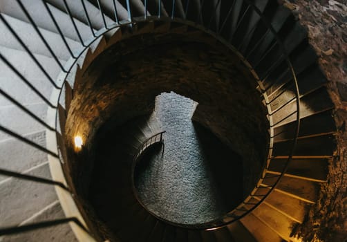 Beautiful view of spiral staircase leading down to exit in observation tower of medieval old castle with modern lamps lighting one spring day, close-up view from top to bottom. Concept historical landmarks, time travel and tourism, ancient architecture.