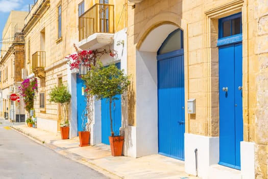 View of an empty typical Maltese street with potted trees near blue wooden garage doors