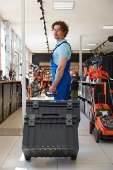 Handyman worker purchasing industrial tools kit at hardware store department. Satisfied repairman pushing trolley cart with new instruments in storage boxes