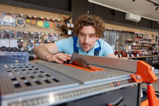 Young man construction worker choosing table circular saw while shopping at power tools shop. Carpenter selecting new machine for cutting wood and woodworks
