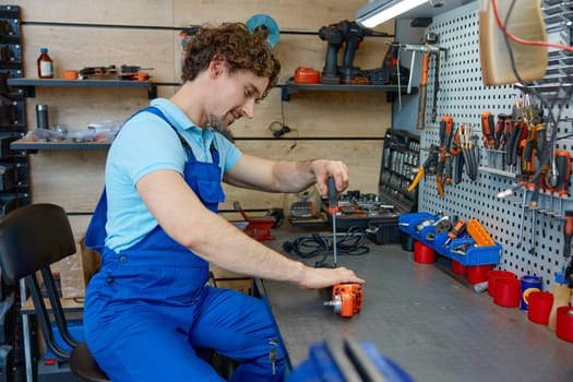 Professional repairman fixing electrical angle grinder working with screwdriver at workshop. Repair shop for broken power tools