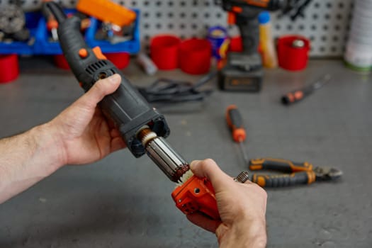 Male repairman fixing electrical angle grinder by replacing motor at workshop. Repair shop for broken power tools