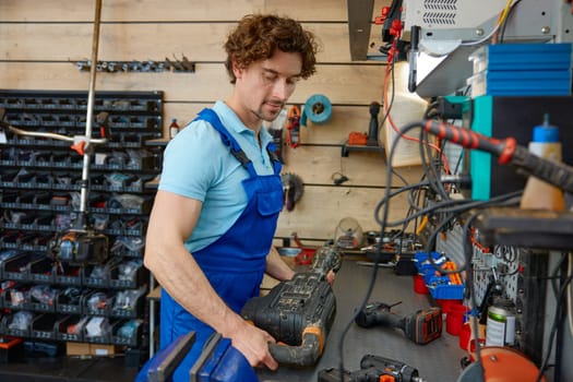 Handyman examining broken perforator power tool before starting to repair. Master providing inspection and inspection of damaged dirty puncher standing at worktable in workshop