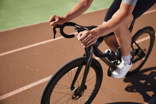 Closeup view on bicyclist holding hands on steering wheel driving bike. Sportsman practicing alone on velodrome enjoying extreme speed riding