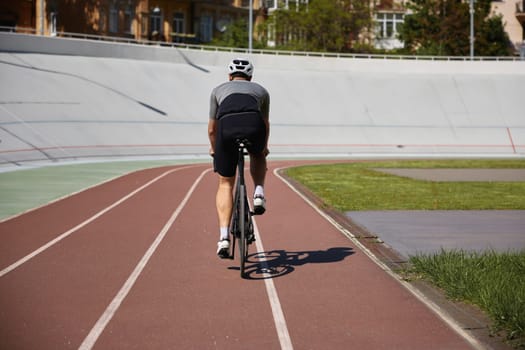 Back view man bicyclist enjoying recreational pursuit riding triathlon bike on empty velodrome road. Active lifestyle and sports hobby concept