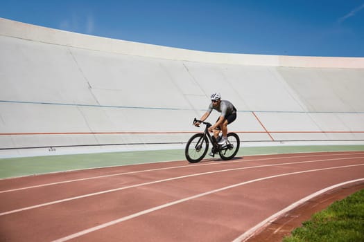 Healthy man cyclist exercising on bicycle on sprint track outdoors. Cycling hobby and training activity concept