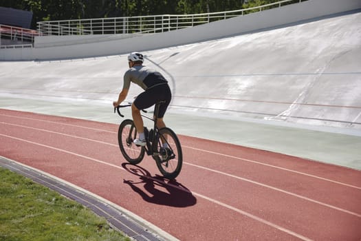 Healthy man cyclist exercising on bicycle on sprint track outdoors. Cycling hobby and training activity concept