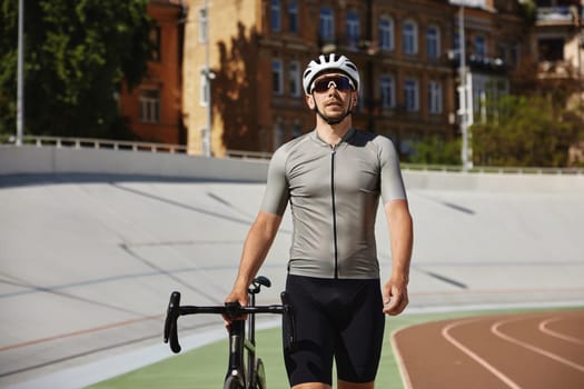 Athletic strong man cyclist wearing professional cycling garment leading bike on side road of sprint track