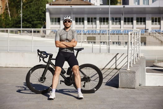 Well-equipped male cyclist wearing activewear, sunglasses and protective headgear came to urban velodrome for training during sunny summer day