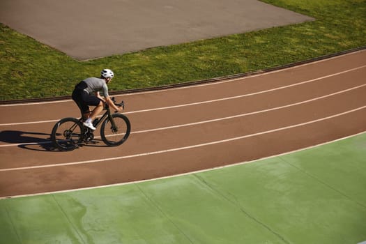 Bicyclist wearing sportive clothing enjoying training cycling on open velodrome track view from afar. Professional sport and hobby recreation concept