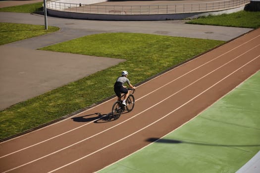 Bicyclist wearing sportive clothing enjoying training cycling on open velodrome track view from afar. Professional sport and hobby recreation concept