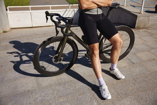 Crop of athletic bicyclist wearing sportswear resting sitting on bike after everyday training workout